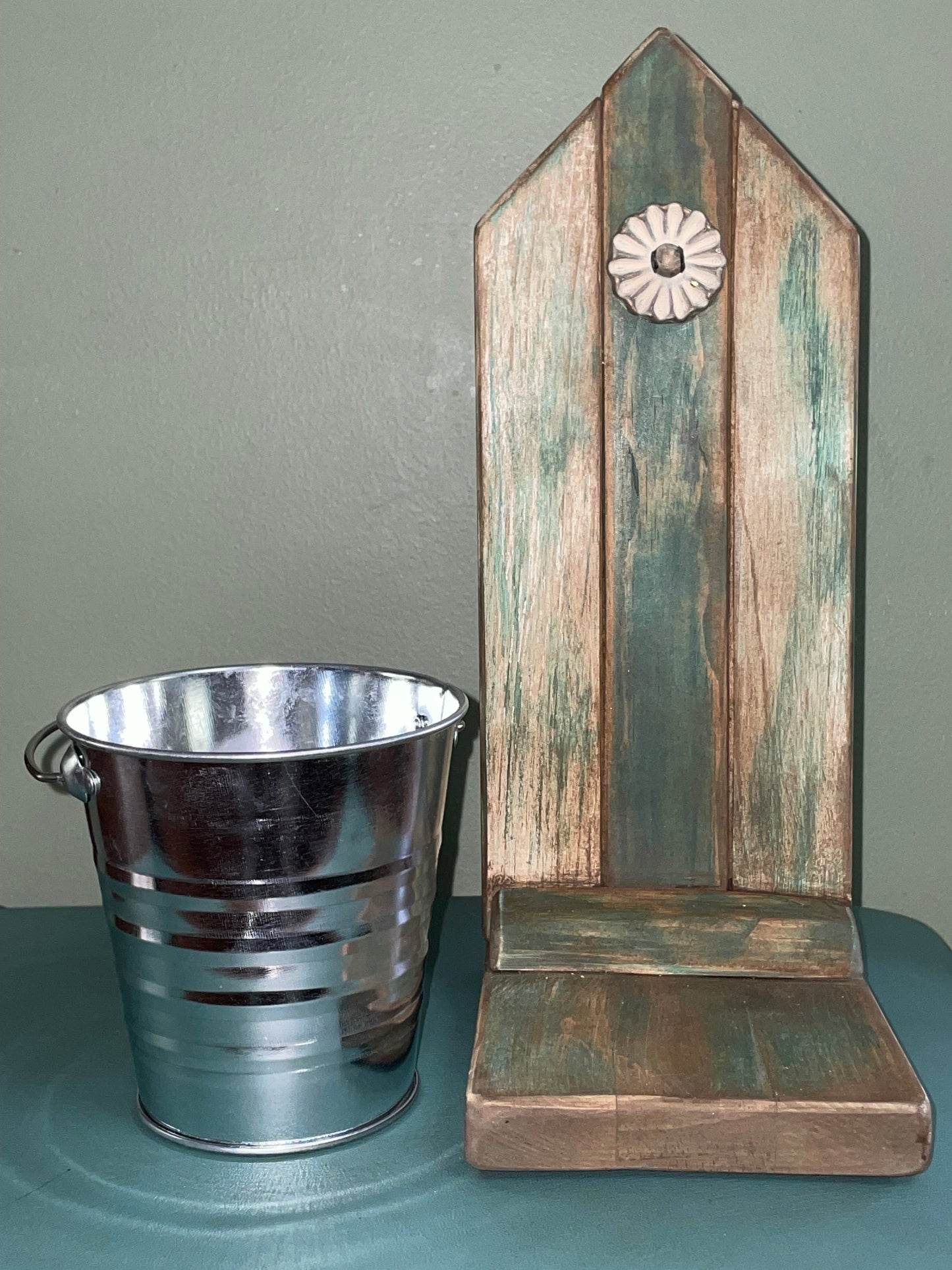 Decorative wooden plant stand with bucket beside and metal accent. 